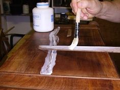 a person is holding a paintbrush over a piece of wood on top of a table