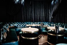 a room filled with lots of blue couches and round tables in front of a black curtain