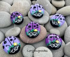 purple ladybug painted rocks sitting on top of some gray rocks with yellow flowers