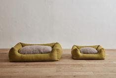 two dog beds sitting on top of a wooden floor next to each other in front of a white wall