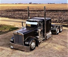 a black semi truck parked on the side of a dirt road next to a field