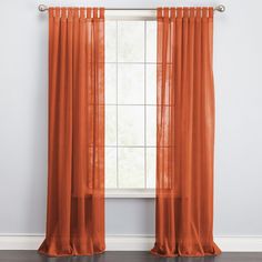 an orange sheer curtain hanging in front of a window with white walls and hardwood floors