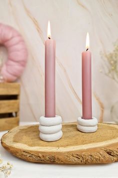 two pink candles sitting on top of a piece of wood next to a white wreath