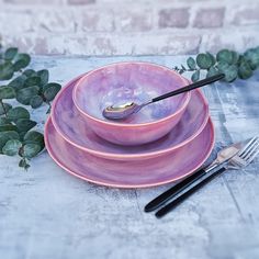 three pink plates and two black forks on a table with green leaves in the background