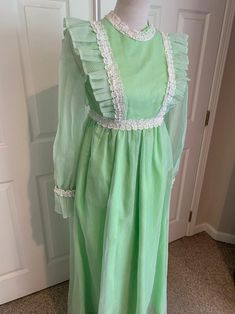 This nice vintage 1970's Mint green & white Swiss Dot and Lace Pinafore dress comes to you in a size small. The dress is a high waist style fully lined-has sheer sleeves and giant ruffle at bottom with lace trim-Has the Pinafore Front-In great vintage cond-Pls compare the measurements I give you to those in your closet-They are as follows- -14 3/4 to 15 inches shoulder to shoulder -25 1/2 inches shoulder to bottom of sleeve -waist is 14 inches across -hips N/A -49 inches underarm to bottom o Green Vintage Ruffled Dress For Spring, Vintage Light Green Dress For Spring, Green Retro Vintage Dress, Vintage Long Sleeve Green Dress, 1970s Housewife, Green Vintage Dress With Ruffles, Retro Green Vintage Dress For Daywear, Green Ruffled Vintage Dress, 1970s Style Fitted Green Maxi Dress