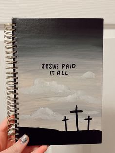 a hand holding up a spiral notebook with the words jesus paid it all