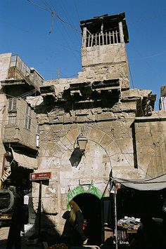 an old stone building with a clock tower on the top and people walking around it