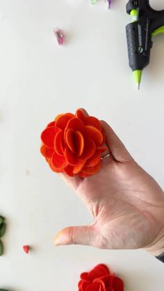 a person's hand holding an orange flower in front of some scissors and other crafting supplies