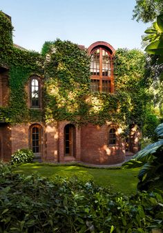 an old brick building with ivy growing on it's walls and windows, surrounded by greenery