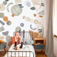 a child laying on top of a bed in front of a wall with circles and shapes