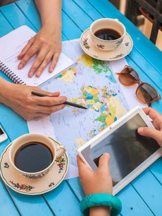 two people sitting at a table looking at a map with a tablet and cup of coffee