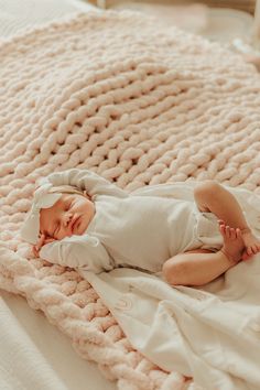 a baby laying on top of a blanket in the middle of a bed with it's eyes closed