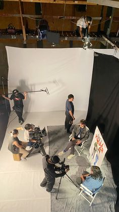 several people sitting in chairs and one person standing behind a camera on a white sheet