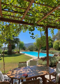 an outdoor dining area next to a swimming pool with trees in the foreground and greenery on either side