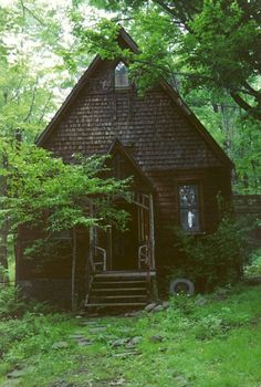 a log cabin in the woods with a green roof and door is surrounded by greenery