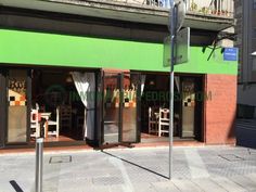 an empty street corner in front of a green building with chairs on the sidewalk outside