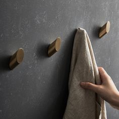 a person is holding a towel in front of two brass hooks on a gray wall