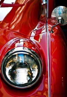 the front end of an old red car with its headlight turned to show it's chrome