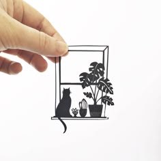 a hand is holding a cutout of a cat and potted plants on a window sill