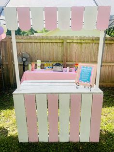 a pink and white ice cream stand on the grass in front of a wooden fence