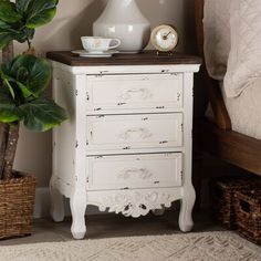 a white chest of drawers next to a potted plant and a clock on top