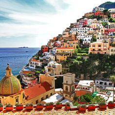 an aerial view of a city with colorful buildings on the cliff above it and blue water in the foreground