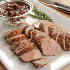 sliced meat on a white plate next to a bowl of sauce