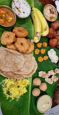 an assortment of food on a banana leaf with sauces, rice and other foods