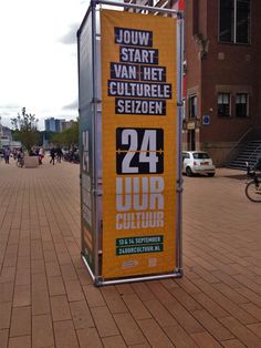 a large sign on the side of a brick road next to a sidewalk with people walking by