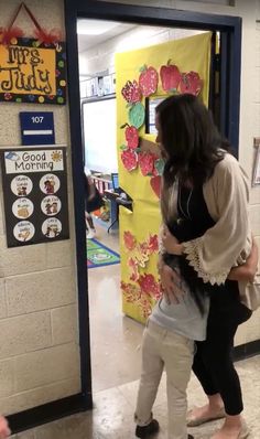 two girls are hugging each other in front of a door decorated with flowers and hearts