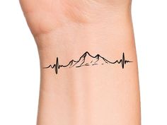 a wrist tattoo with mountains and heartbeats on the back of it's arm