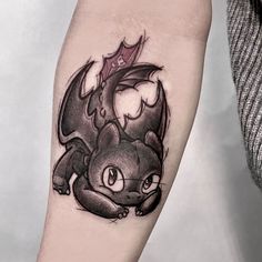 a black and white photo of a cat tattoo on the left arm, with a bat in it's claws