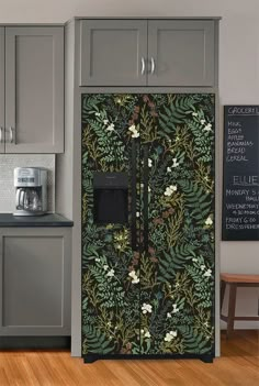 a kitchen with grey cabinets and a black floral wallpaper on the side of the refrigerator