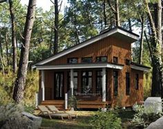 a small wooden cabin in the woods surrounded by rocks and trees with two lounge chairs on the lawn