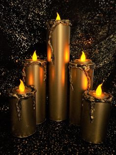 five lit candles sitting next to each other on a black counter top with gold flecks