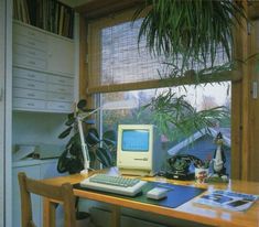 an old computer sitting on top of a wooden desk next to a potted plant