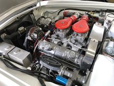 the engine compartment of a silver car with two red valve covers on it's hood