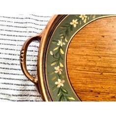 an oval wooden tray with flowers painted on the sides and gold trimming around it