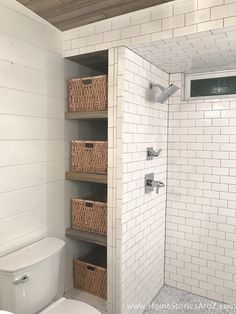 a white toilet sitting in a bathroom next to a walk in shower with wicker baskets