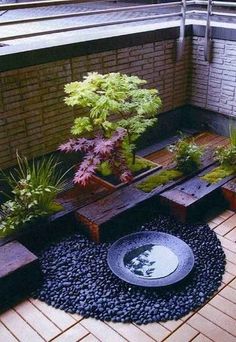 an outdoor patio with wooden benches, plants and gravel on the ground in front of a brick wall