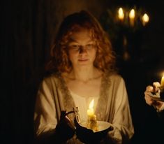 a woman holding a lit candle in her hands and looking down at the plate she is holding