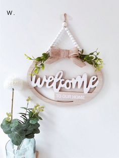 a welcome sign hanging on the wall next to a vase with flowers and a potted plant