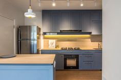 an empty kitchen with blue cabinets and stainless steel appliances in the center, along with wooden flooring