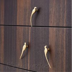 three birds are standing on the handles of a wooden dresser drawer, one is gold and the other is dark wood