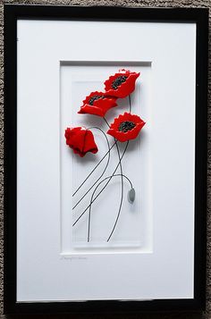 three red flowers in a white frame on the wall next to a black and white object