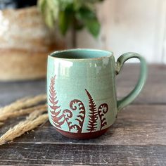 a green cup with red designs on it sitting on a table next to a plant