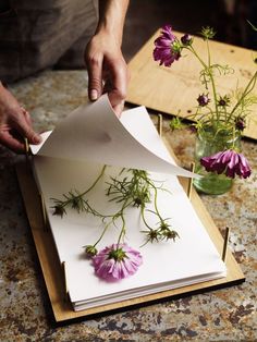 a person cutting paper with flowers in vases on the table next to each other