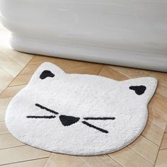 a white rug with a black cat's face on the floor next to a bathtub