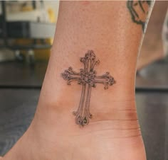 a cross tattoo on the foot of a woman's ankle is shown in this image