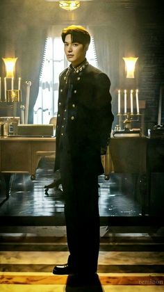 a man standing in front of a table with candles on it and wearing a black coat